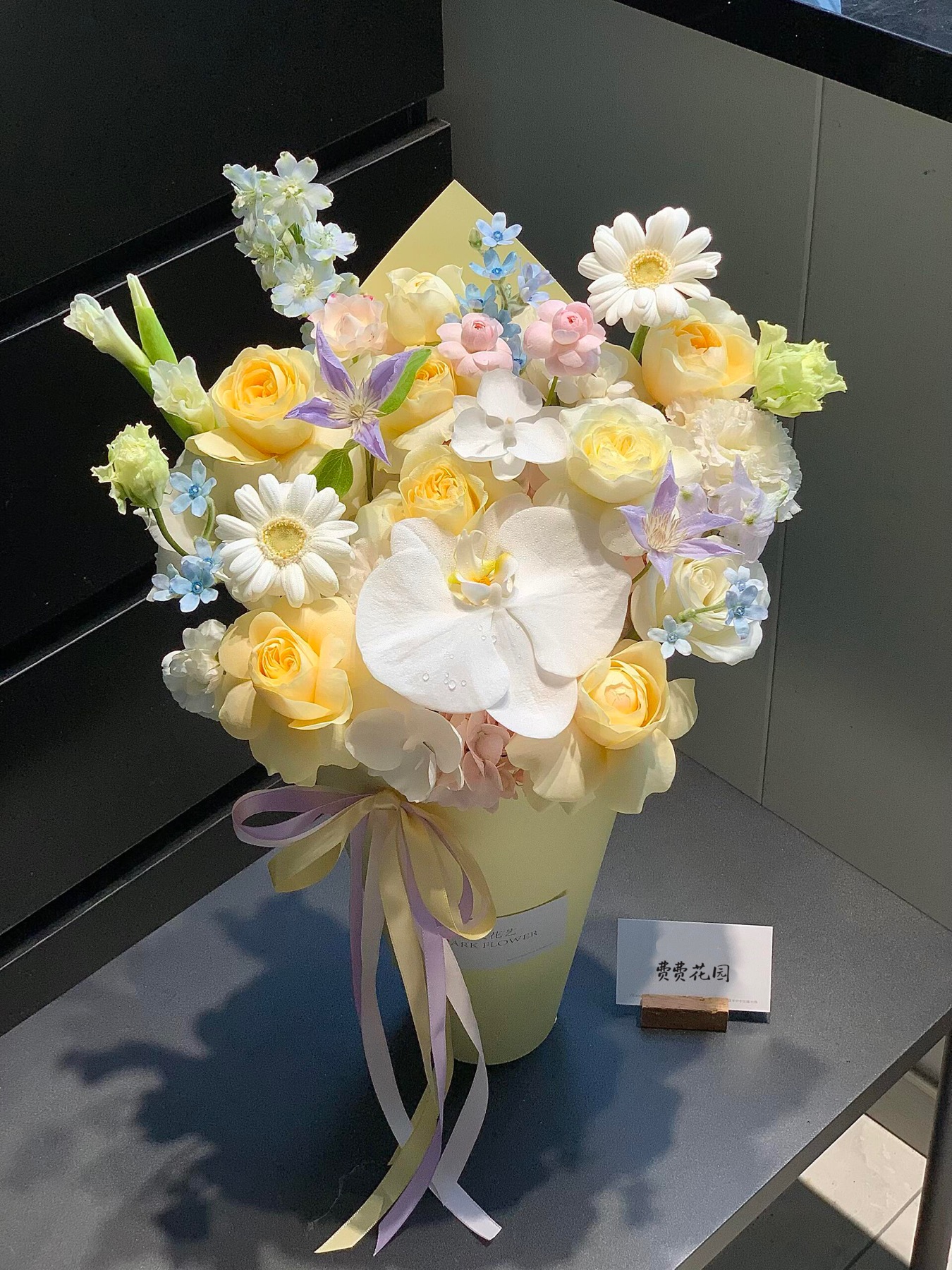 杭州教师节奶黄蝴蝶兰花桶近景，白色蝴蝶兰、奶黄玫瑰、扶郎和浅蓝小花组合